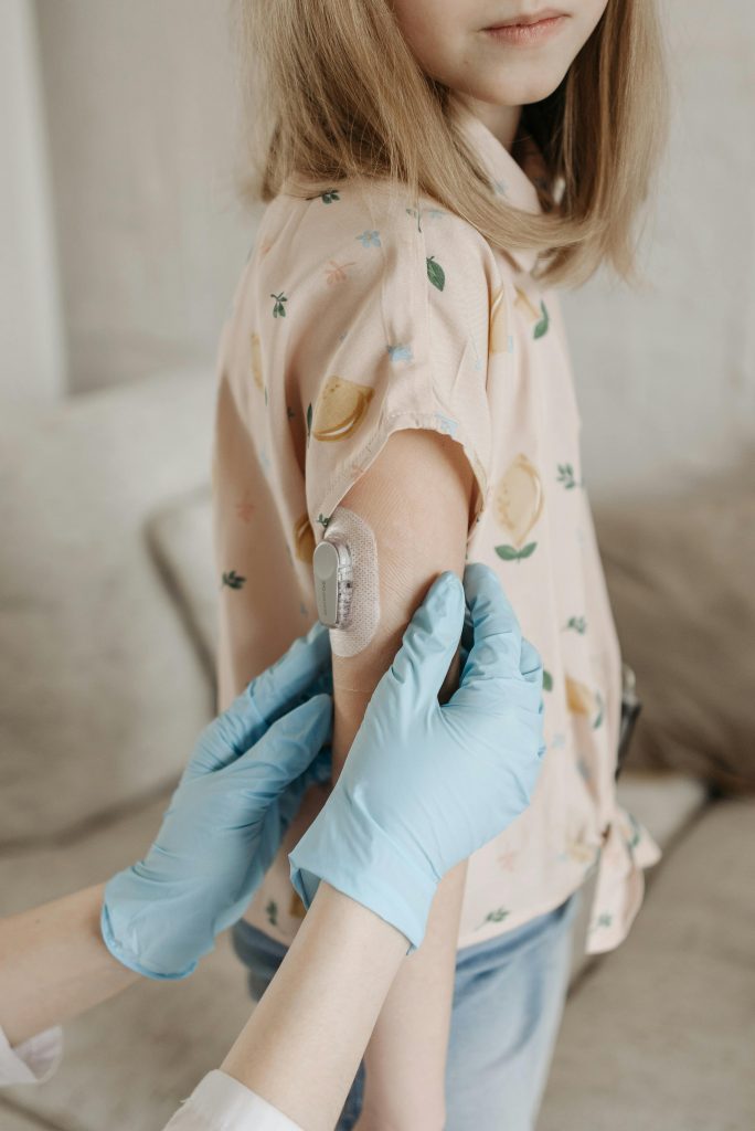 Sinais de diabetes em crianças: profissional de saúde aplicando sensor de glicose no braço de uma criança para monitoramento da glicemia.