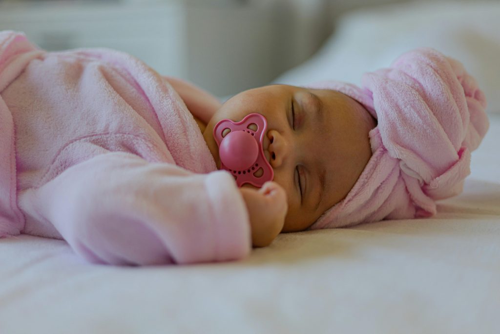 Danos causados pela chupeta. Peaceful newborn baby sleeping in pink attire with a pacifier. Inicio de danos causados pela chupeta